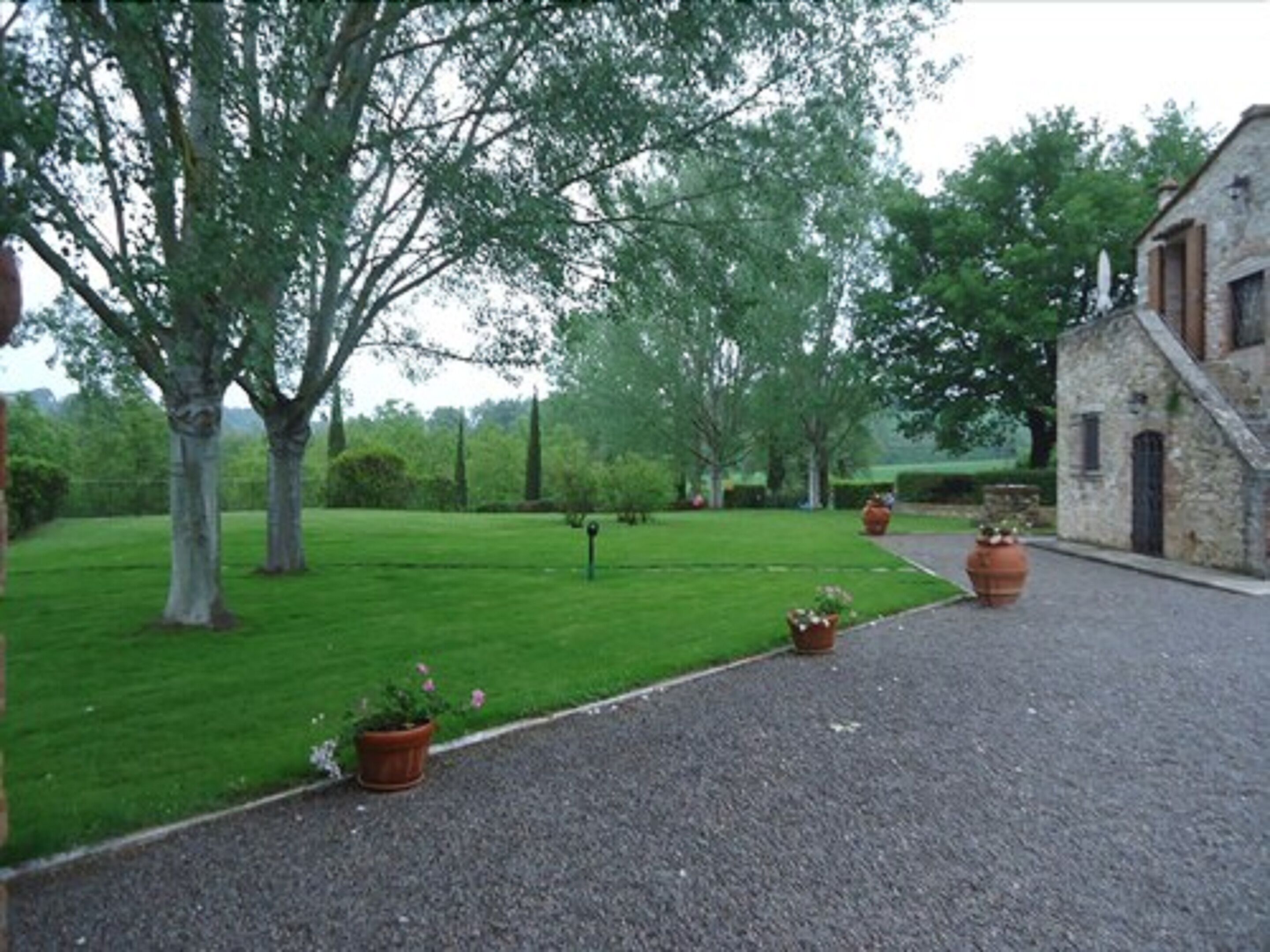 A gravel driveway leading to a stone building with a sloped roof, surrounded by a well-maintained lawn and trees.