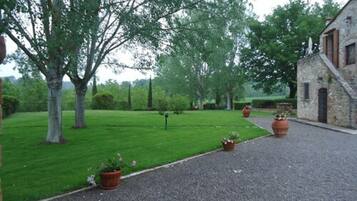 A gravel driveway leading to a stone building with a sloped roof, surrounded by a well-maintained lawn and trees.