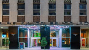 A hotel entrance with a modern design, featuring a large glass facade, a tree in the center, and a neon-lit canopy above the entrance. - Aloft by Marriott New Orleans Downtown (New Orleans)