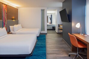 Une chambre d’hôtel avec deux lits, un bureau, une chaise, une télévision et une salle de bain visible à travers une porte ouverte.