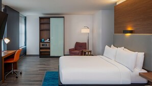 A hotel room with a large bed, a desk with a chair, a small table, a lamp, and a wardrobe. - Aloft by Marriott New Orleans Downtown (New Orleans)