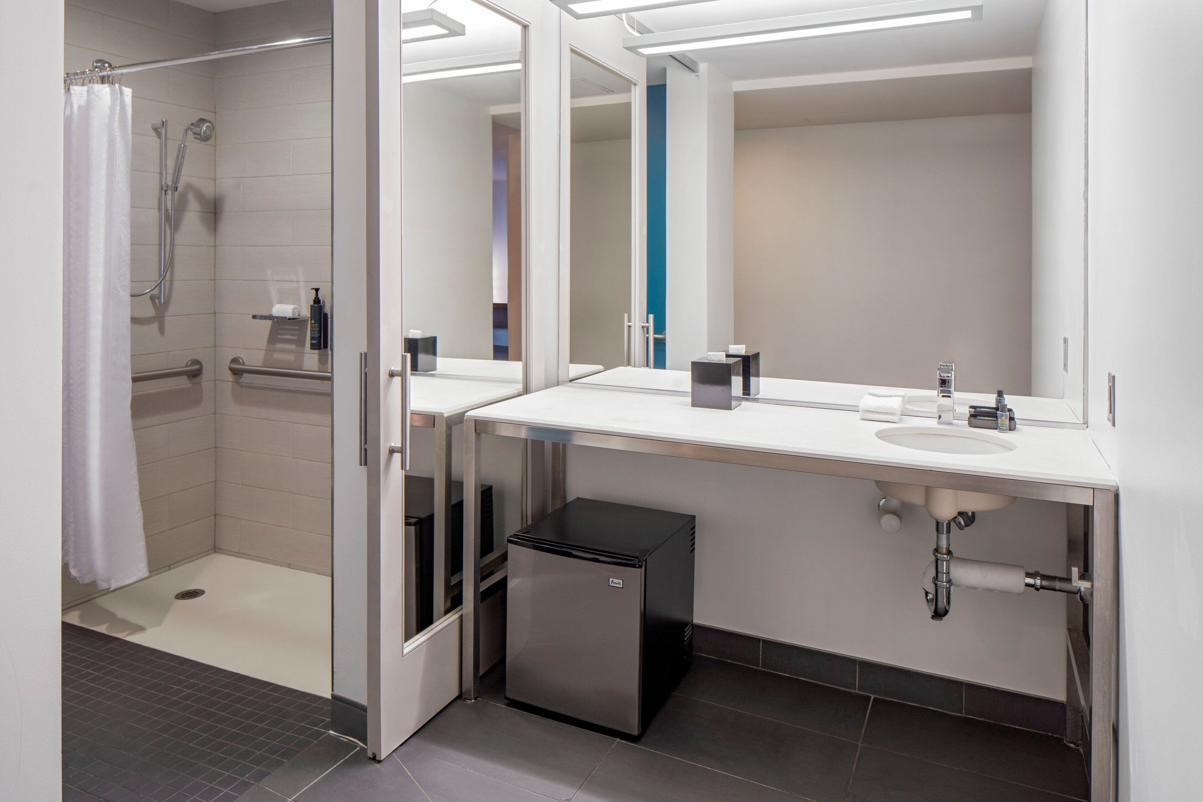 A modern bathroom with a shower, a sink, and a compact trash bin.
