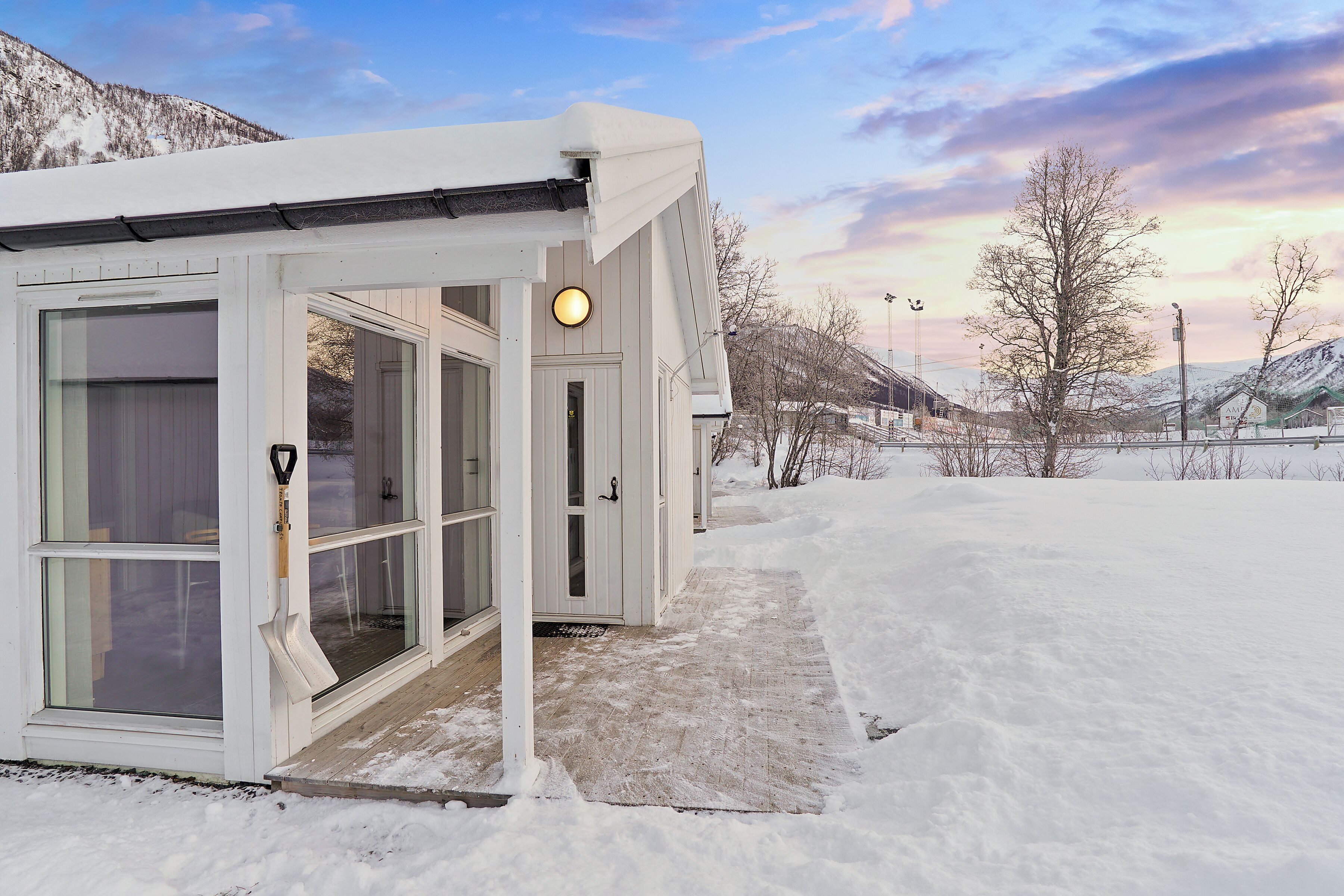 A snow-covered building with large windows and a door, surrounded by a snowy landscape and mountains.