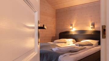 Un dormitorio con techo de madera, una cama con cabecera oscura y dos luces fijadas a la pared.