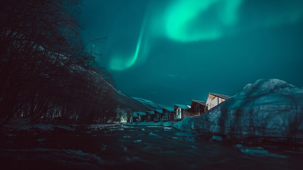 A row of cabins by a river with a view of the northern lights. - Tromsø Lodge & Camping (Tromsø)