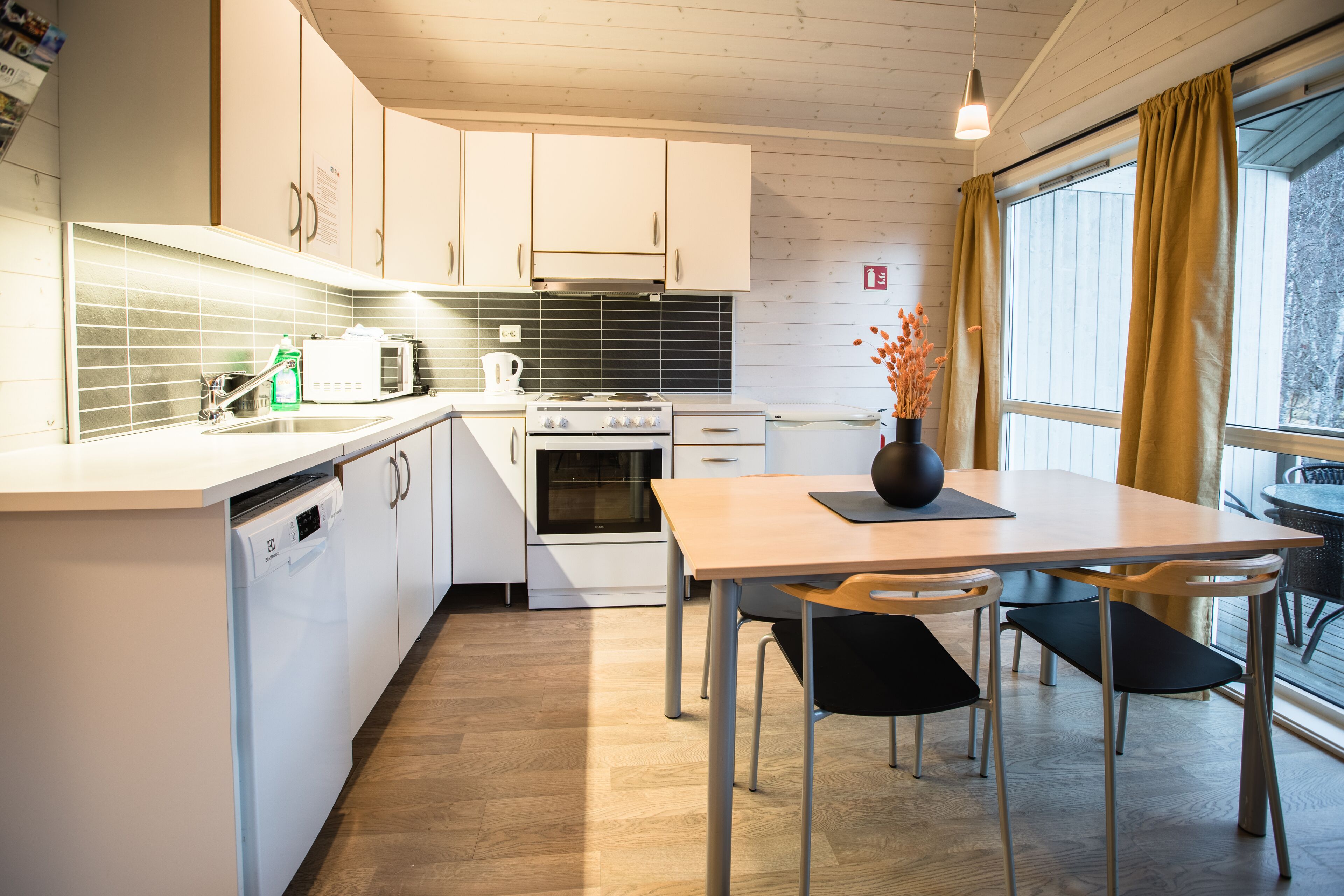 Una cocina moderna con armarios blancos, lavavajillas, estufa y un comedor con mesa y sillas.