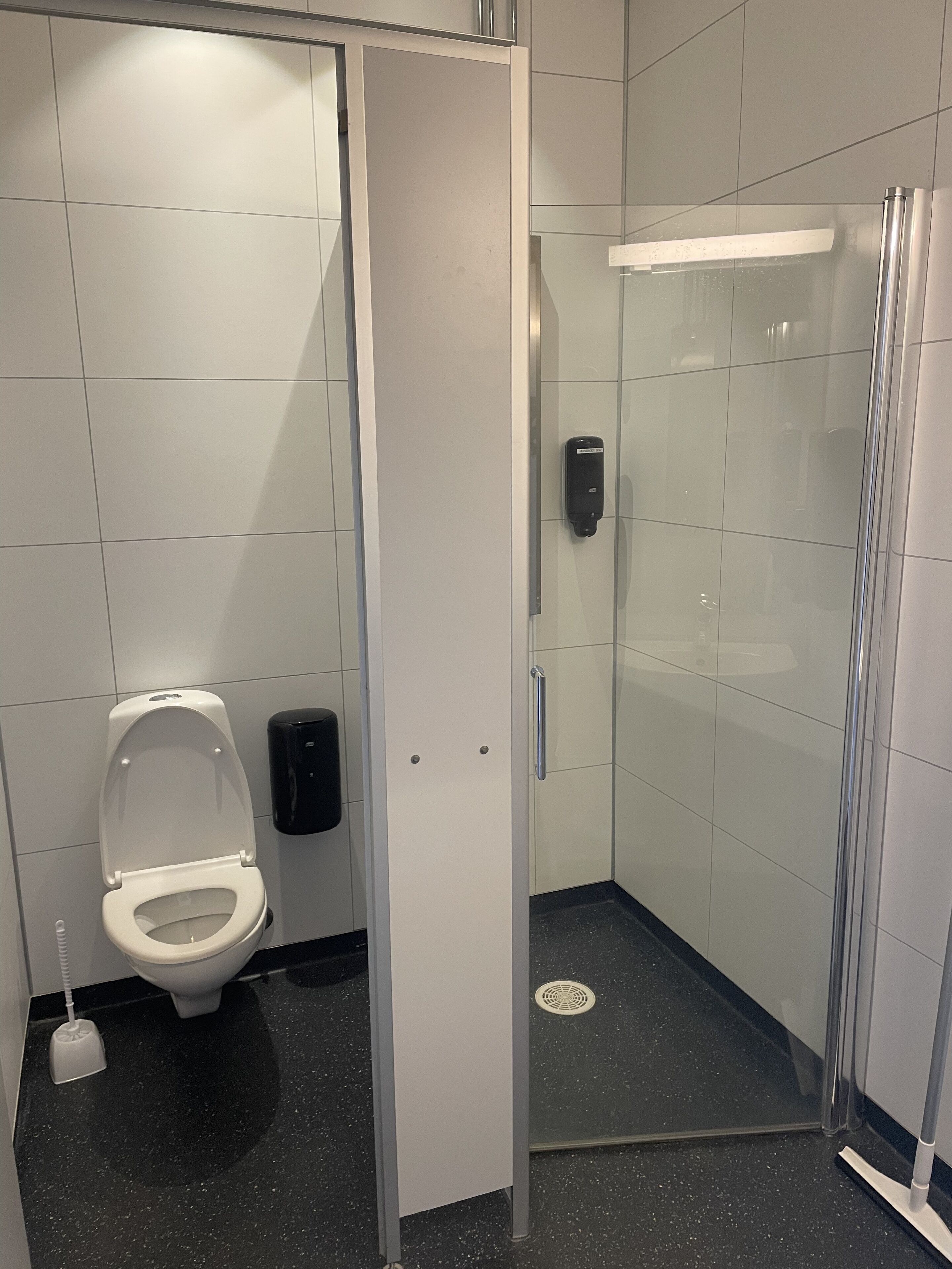 Une salle de bain moderne équipée de toilettes, d’un sèche-mains et d’une cabine de douche en verre.