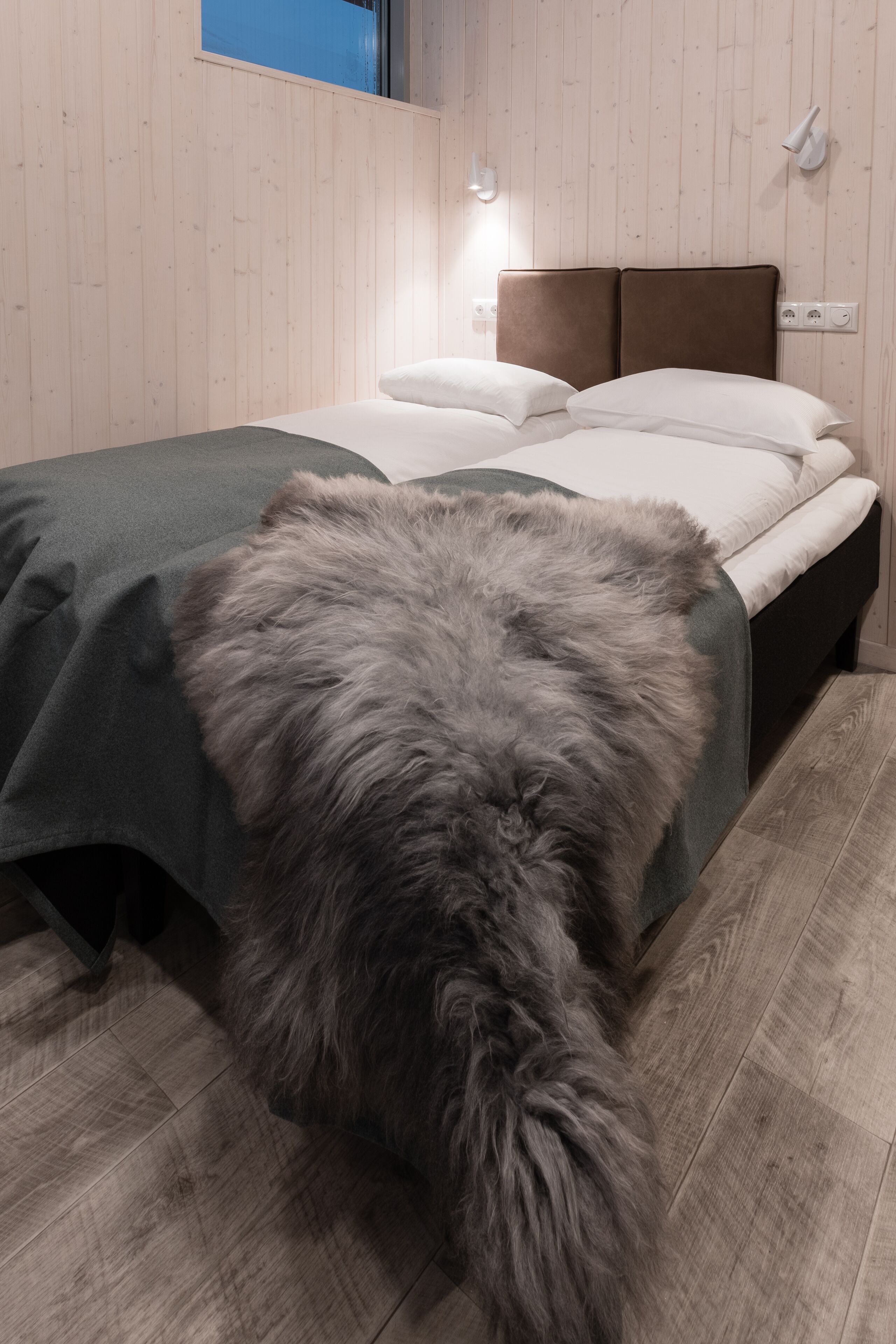 A bedroom with a wooden floor, a bed with a dark headboard, and a fluffy gray rug.