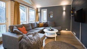A modern living room with a sectional sofa, a round coffee table, and a flat-screen TV mounted on the wall. - Tromsø Lodge & Camping (Tromsø)