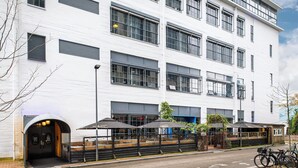 A modern multi-story building with a white facade, large windows, and outdoor seating areas with umbrellas. - Stayokay Eindhoven - Hostel (Eindhoven)