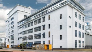 A multi-story building with a white facade, large windows, and a clock tower. - Stayokay Eindhoven - Hostel (Eindhoven)