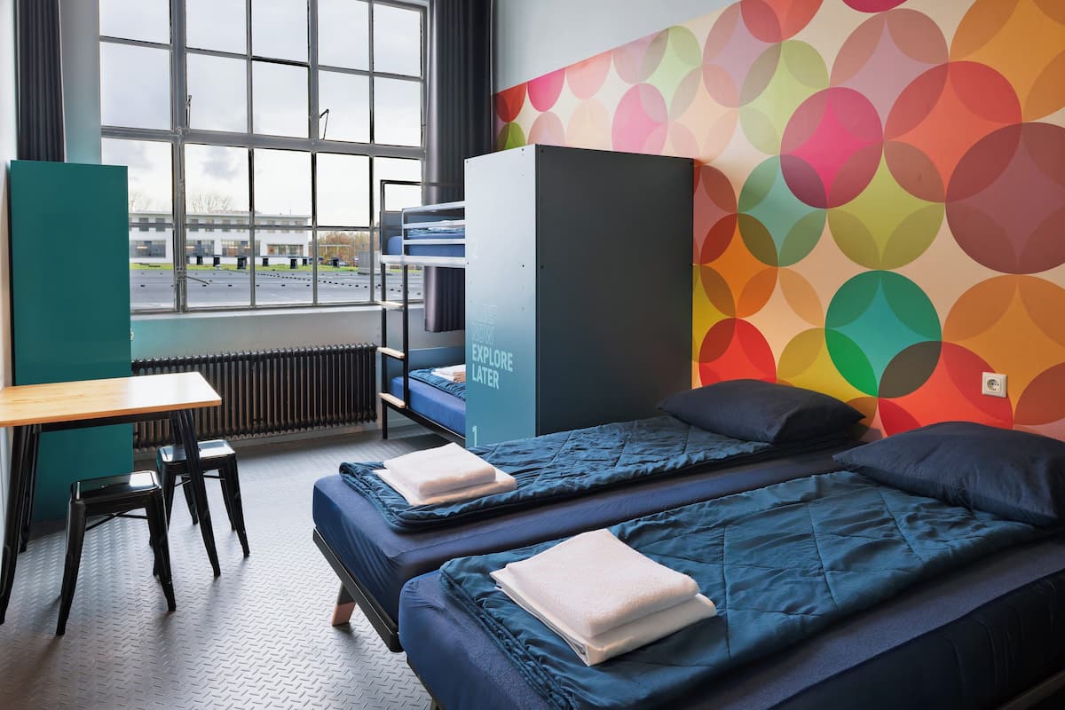 A dormitory room with two beds, a desk, and a window.