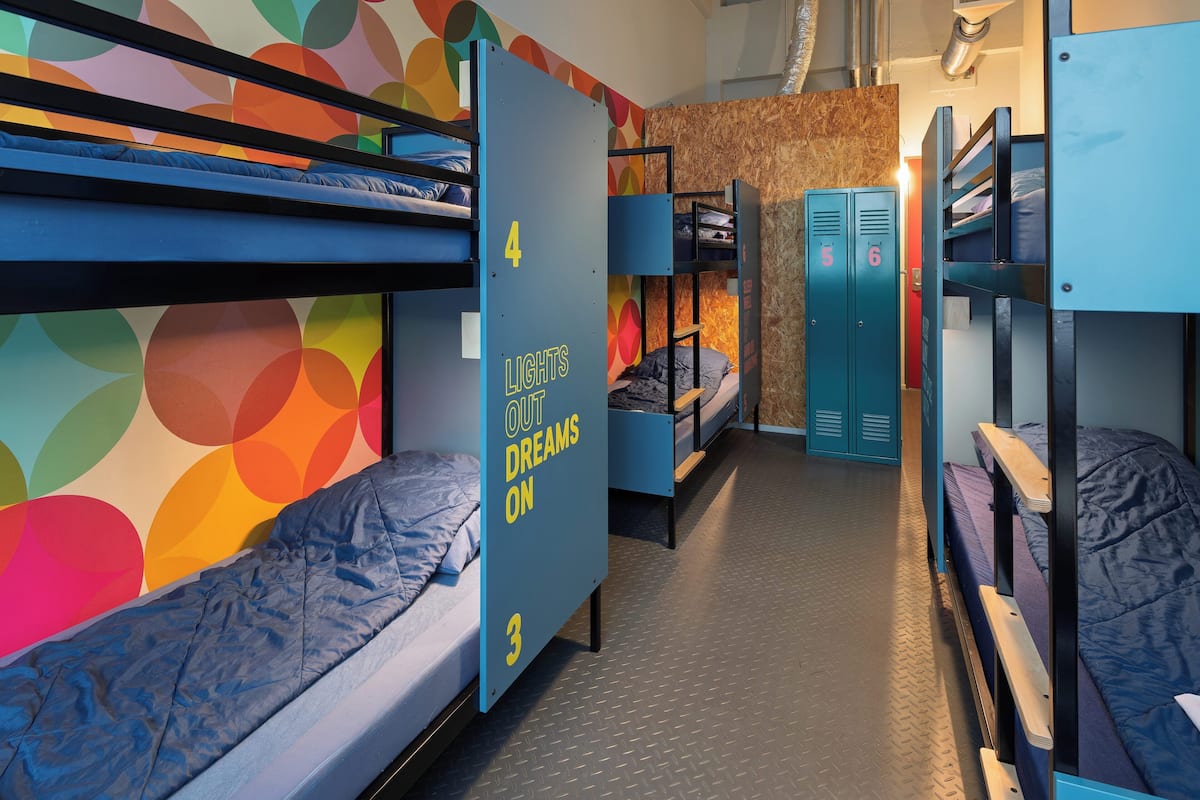A dormitory room with bunk beds, lockers, and a colorful wall design.