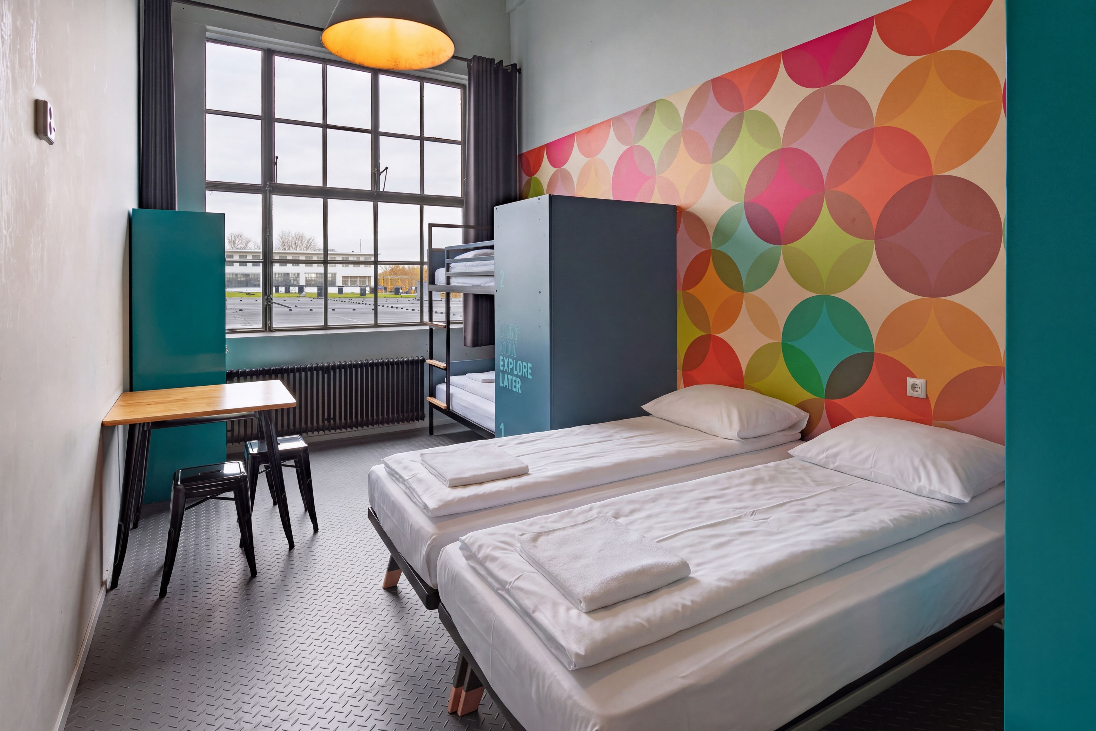 A room with two beds, a desk, and a window with a view of a parking lot.