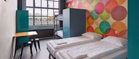 A room with two beds, a desk, and a window with a view of a parking lot.