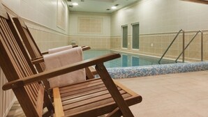 A wooden chair with a towel, a pool, and a tiled wall.