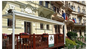 A wooden bench with a sign in front of a building with ornate architecture and balconies.