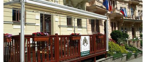 A wooden bench with a sign in front of a building with ornate architecture and balconies.