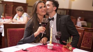 A couple at a restaurant table with a candle, wine glasses, and a red tablecloth.