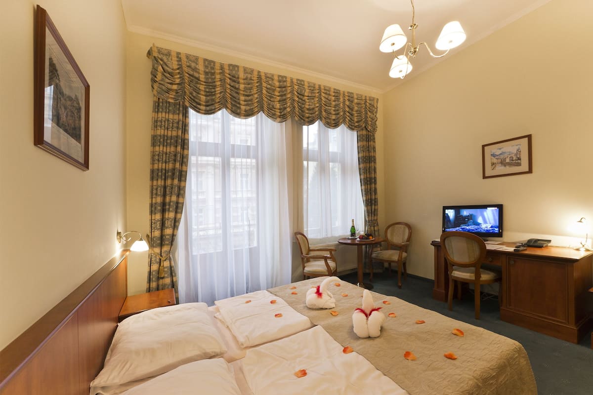 A hotel room with a large bed, a desk with a computer, a chair, and a television.