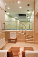 A hotel bathroom with a glass-enclosed shower area, a wooden bench, and a tiled floor.