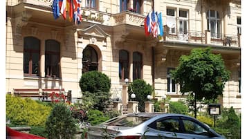 A historic building with multiple flags, a car, and lush greenery.