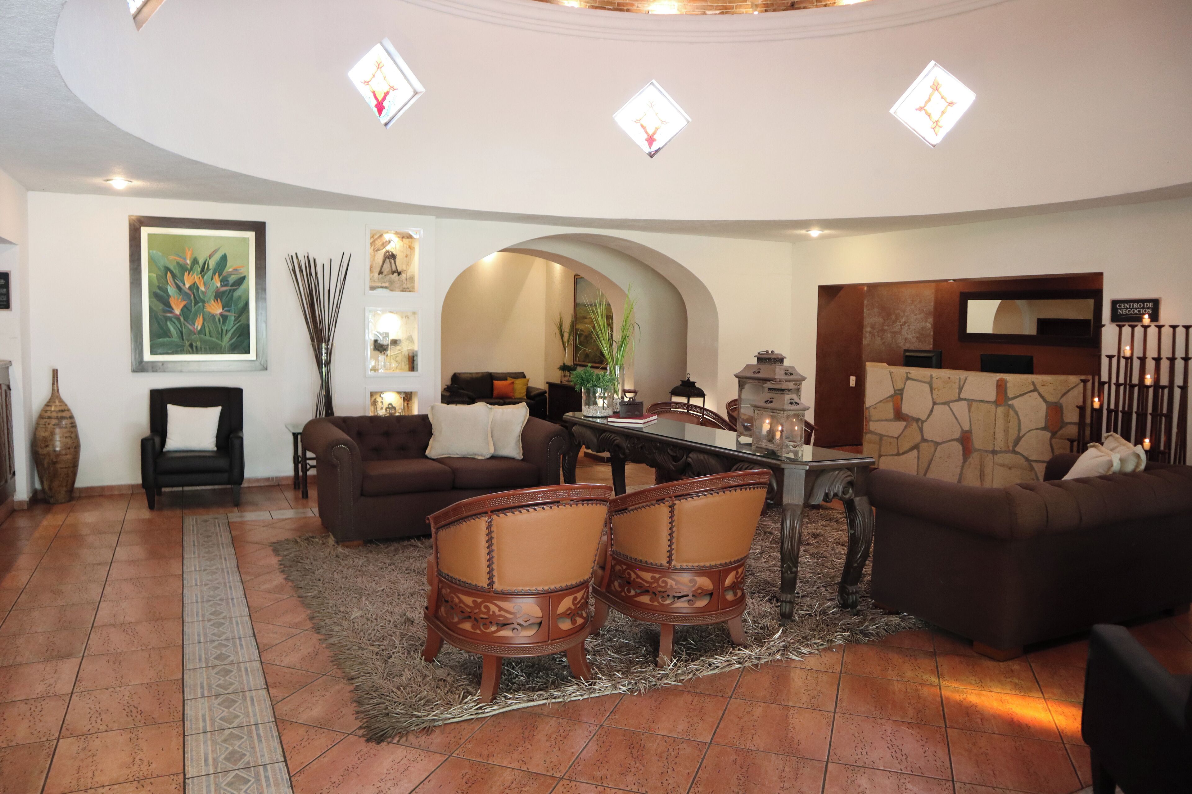 A spacious living area with a dining table, two sofas, and a coffee table. There is a large painting on the wall and a mirror above the fireplace.
