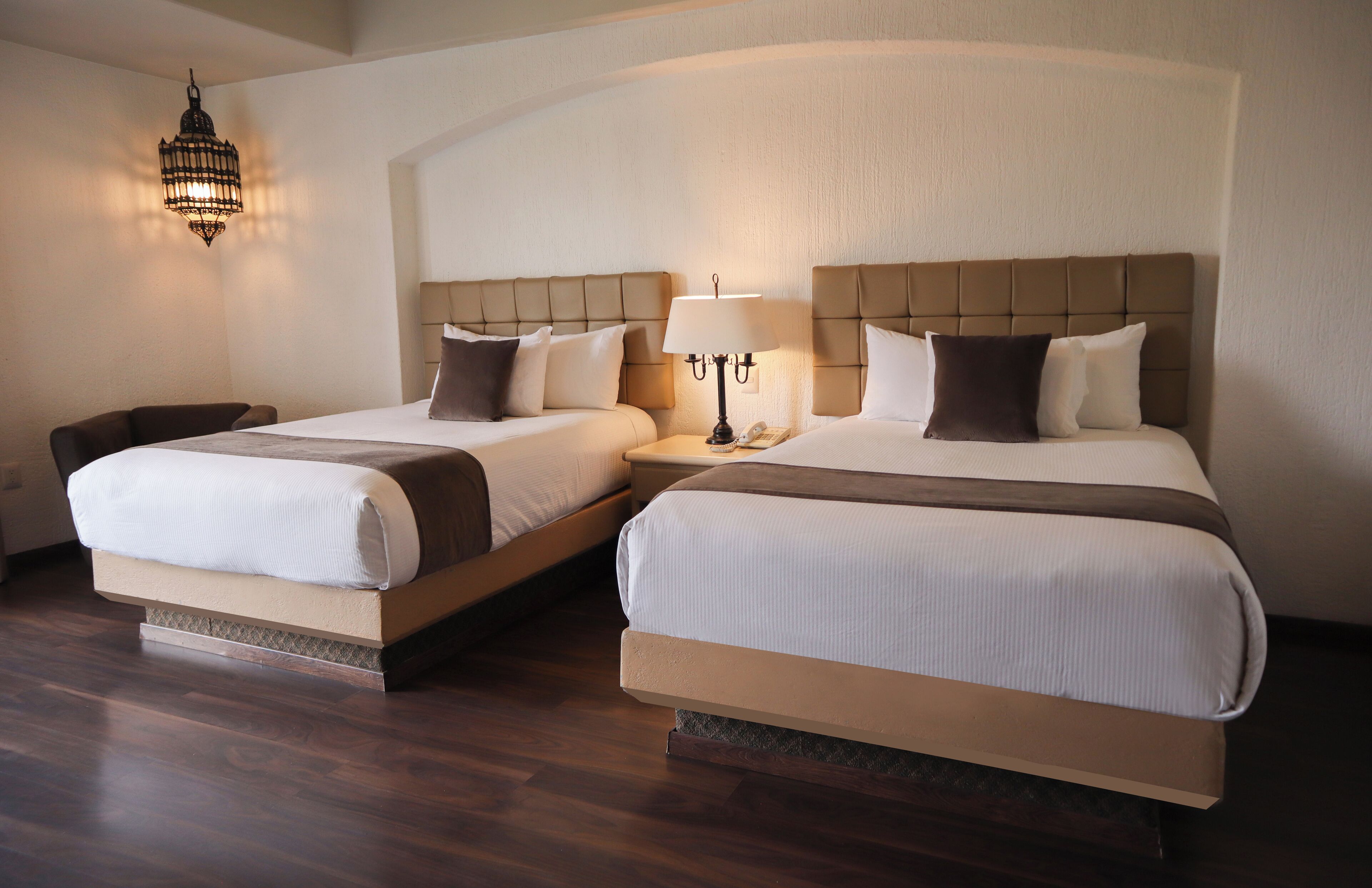 Two double beds with headboards, a bedside table with a lamp, and a hanging light fixture.