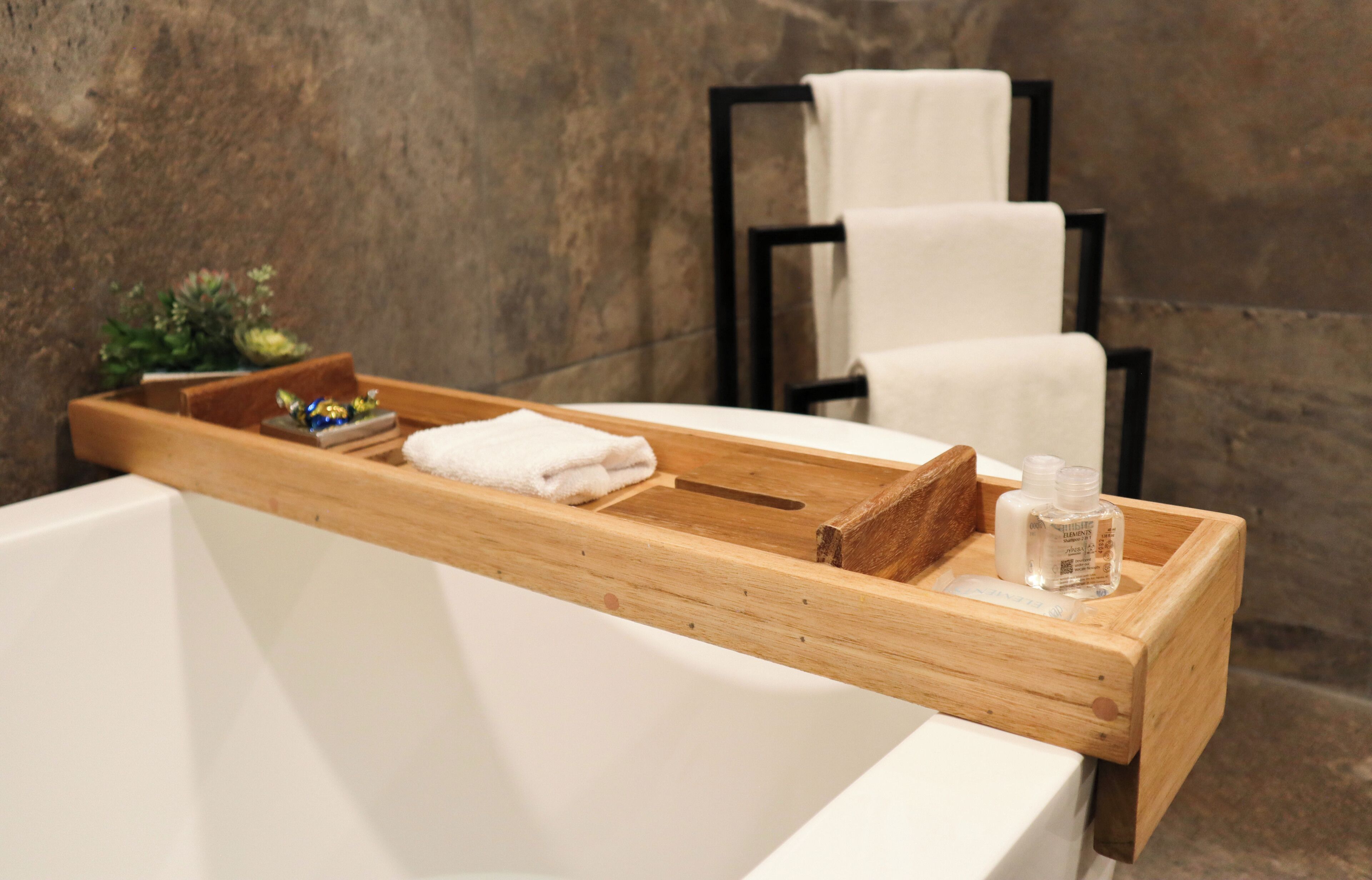 A wooden tray with towels and toiletries on a bathtub.