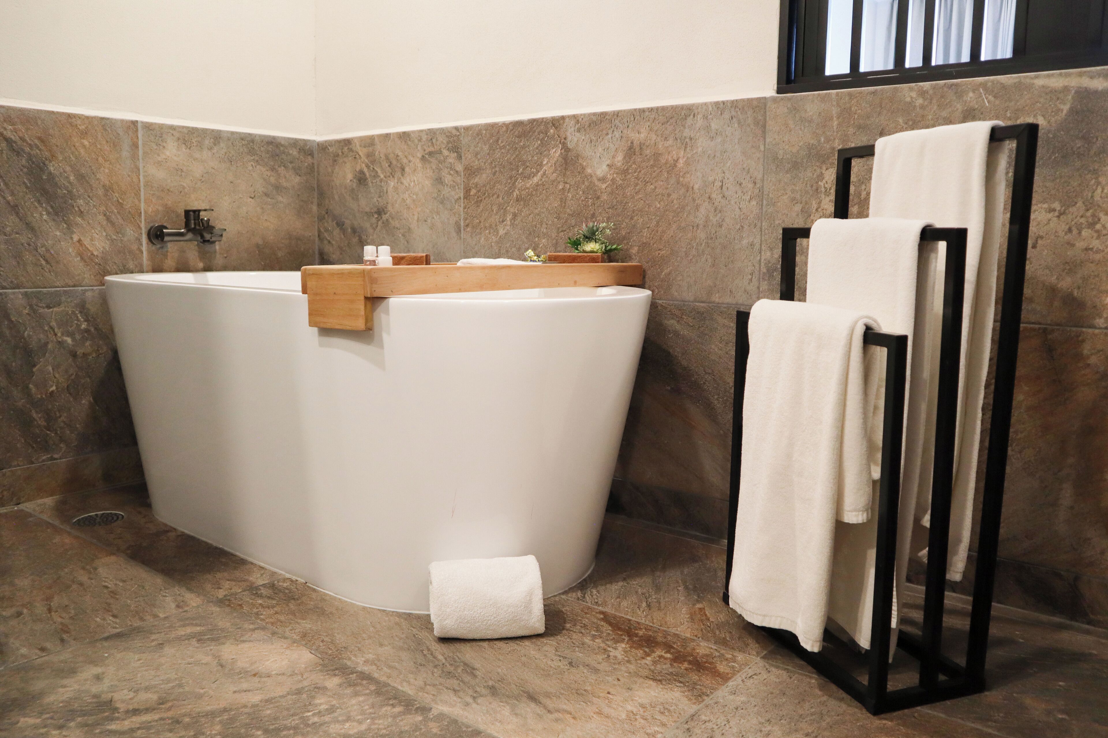 A modern bathroom with a freestanding bathtub, a wooden shelf with toiletries, and a towel rack with folded towels.