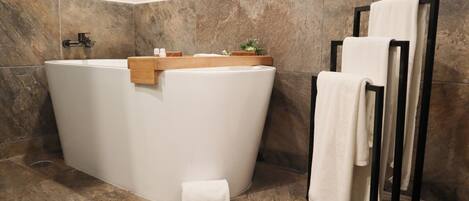 A modern bathroom with a freestanding bathtub, a wooden shelf with toiletries, and a towel rack with folded towels.