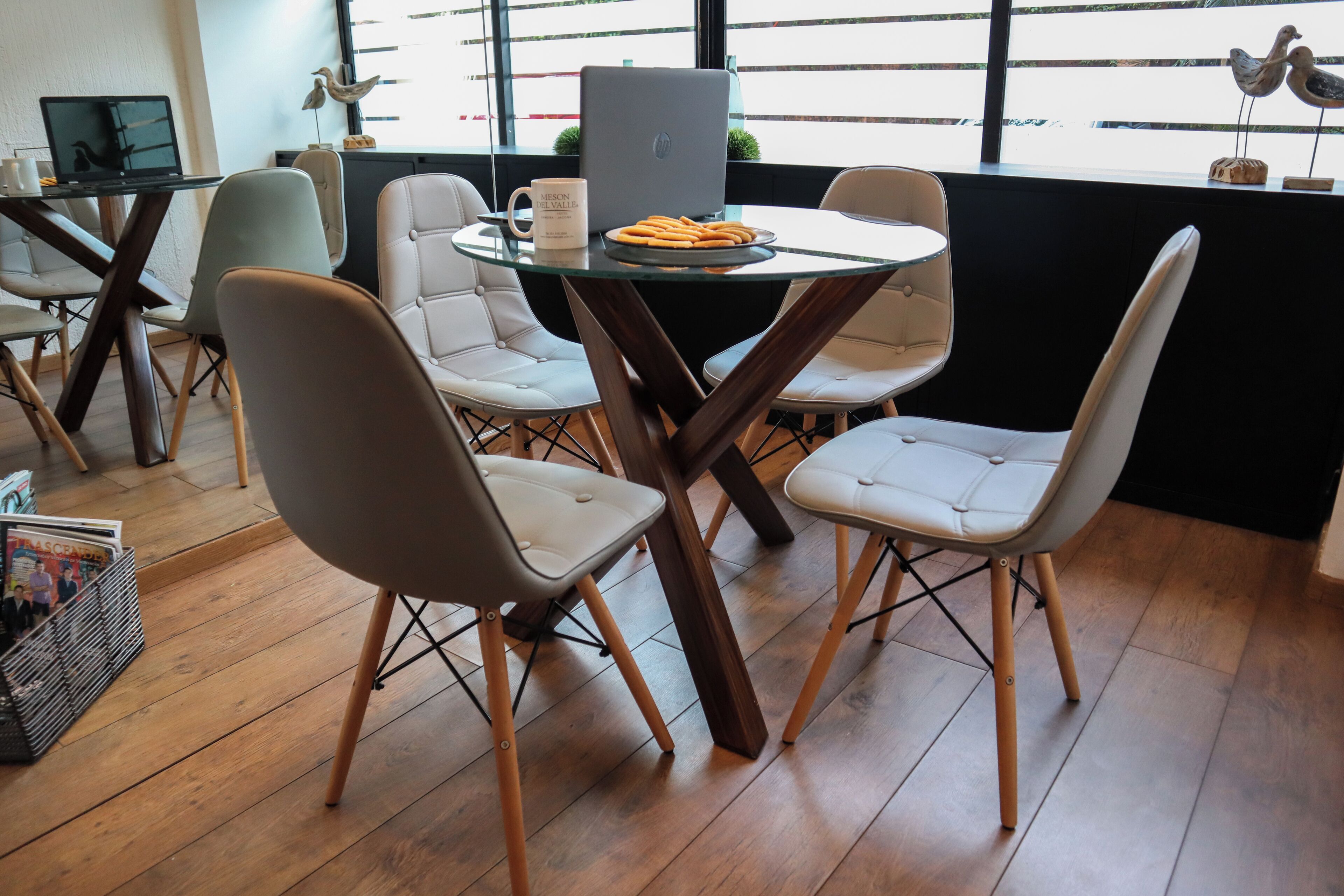 Un área de comedor moderna con una mesa de vidrio, cuatro sillas y una laptop sobre la mesa.