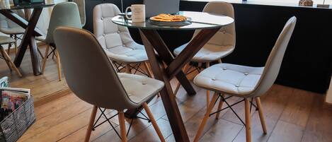 Un área de comedor moderna con una mesa de vidrio, cuatro sillas y una laptop sobre la mesa.