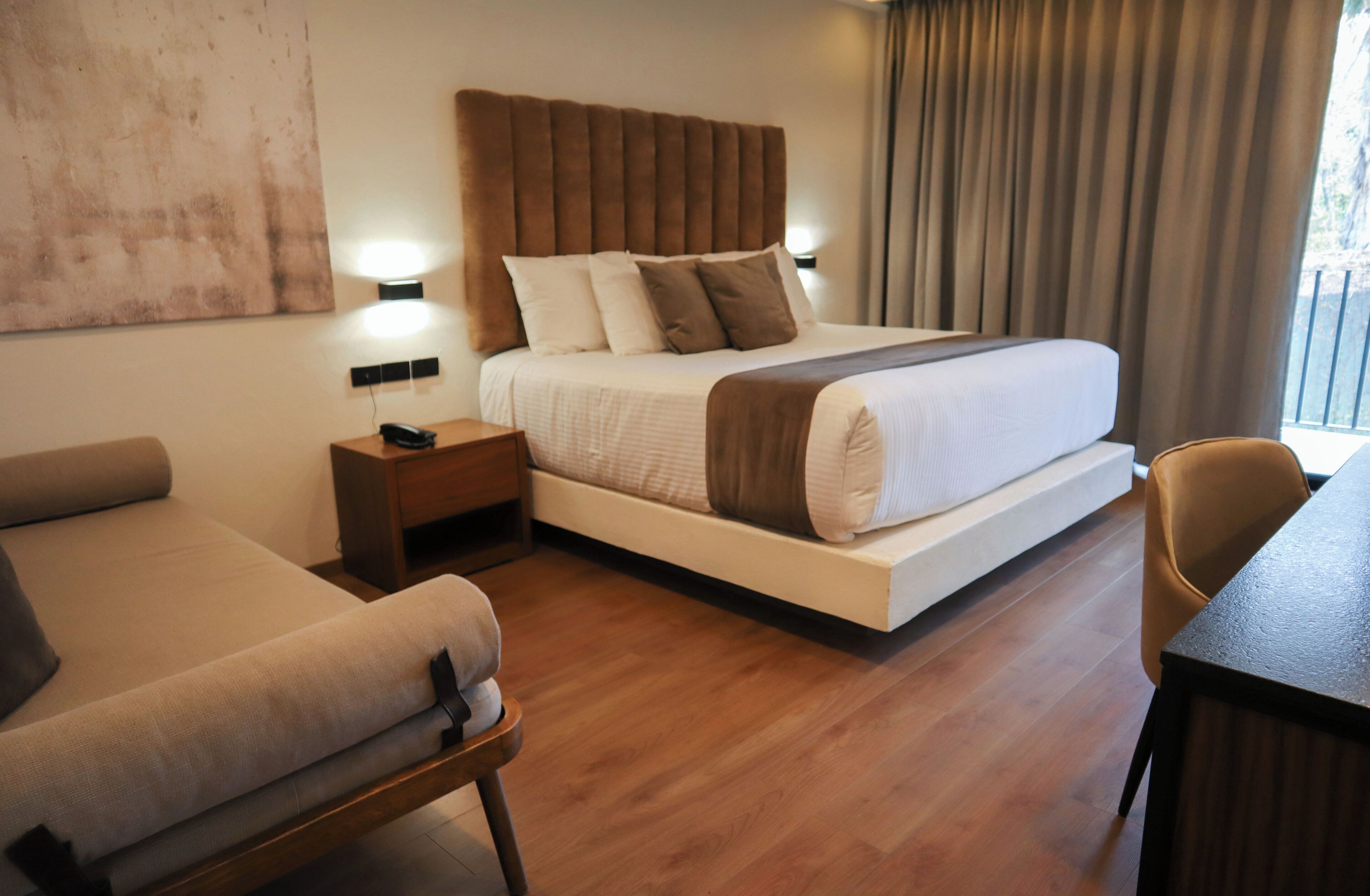 Una habitación de hotel moderna con una cama grande, una mesita de noche con teléfono, un sofá y una mesa de comedor.