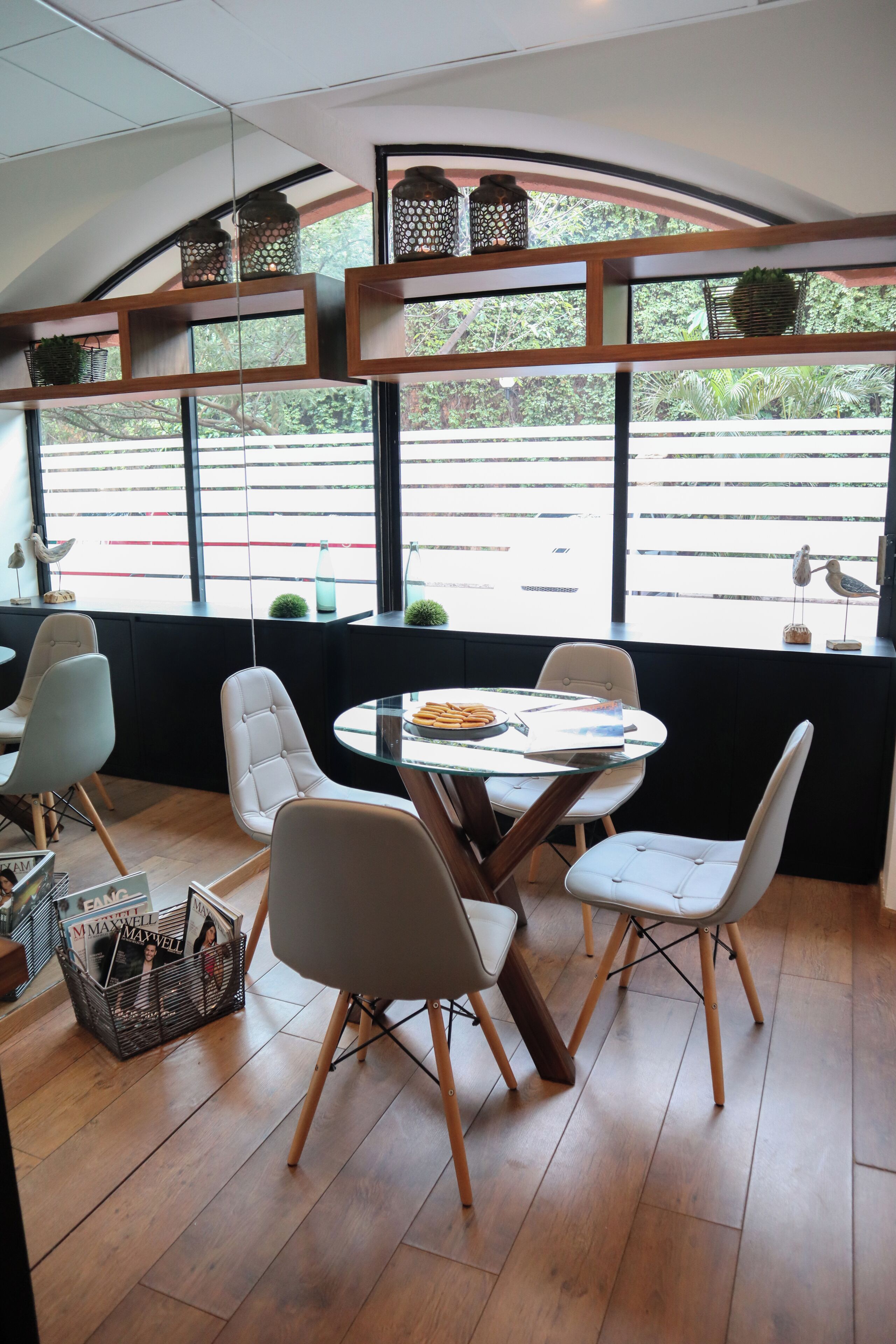 Un comedor moderno con una mesa redonda, sillas blancas tapizadas y vistas a la calle a través de amplias ventanas.
