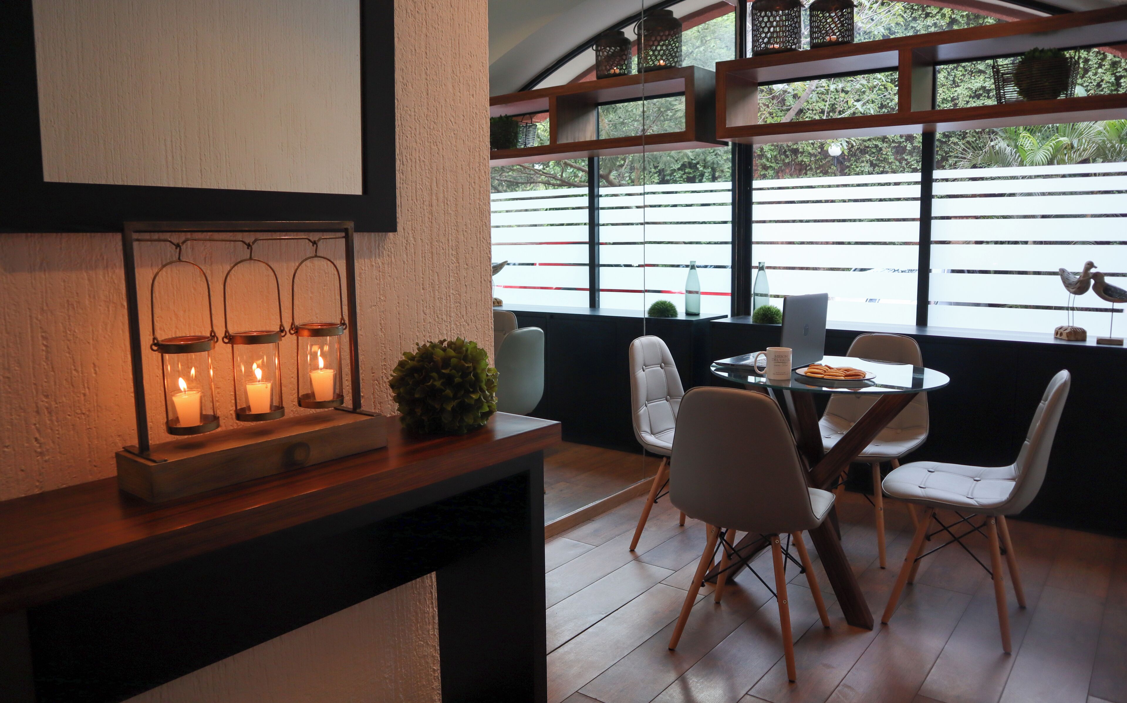 Un comedor con una mesa y sillas, una estantería con velas y vistas al exterior.