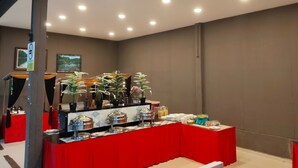 A buffet setup with a red table, various food containers, and potted plants.