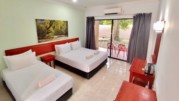 A hotel room with two beds, a small table, a chair, and a window with curtains.
