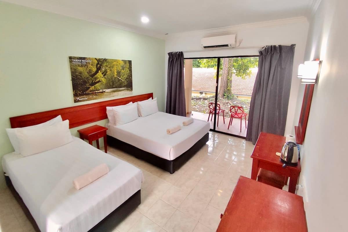 Habitación de hotel con dos camas, una mesita, una silla y un ventanal con cortinas.