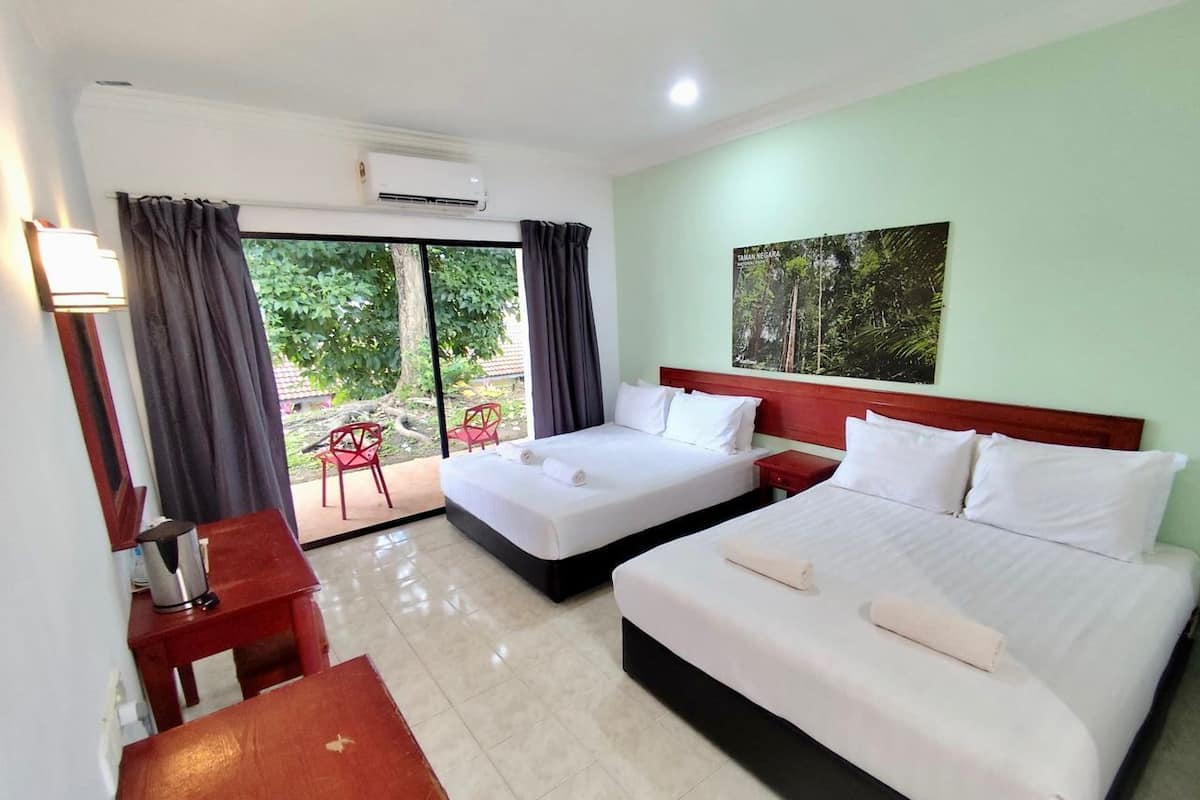 Habitación de hotel con dos camas, un escritorio, una silla y un ventanal con cortinas.