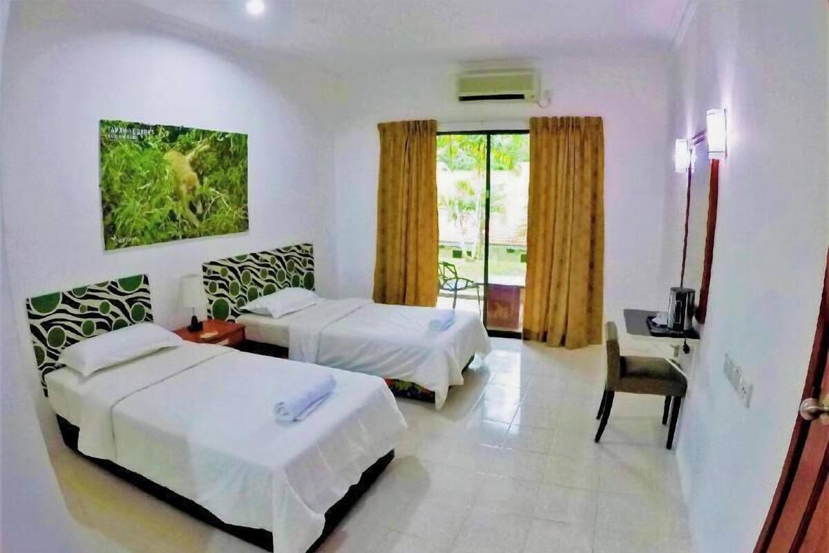 Habitación de hotel con dos camas, un escritorio, una silla, un ventanal con cortinas, un equipo de aire acondicionado y un cuadro colgado en la pared.