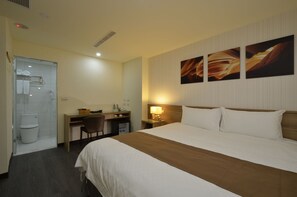 Habitación de hotel con cama, escritorio, silla y zona de ducha.