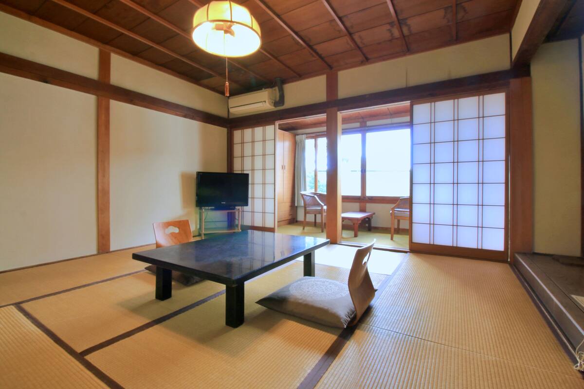 A tatami mat room with a low table, a television, and sliding doors leading to a balcony.