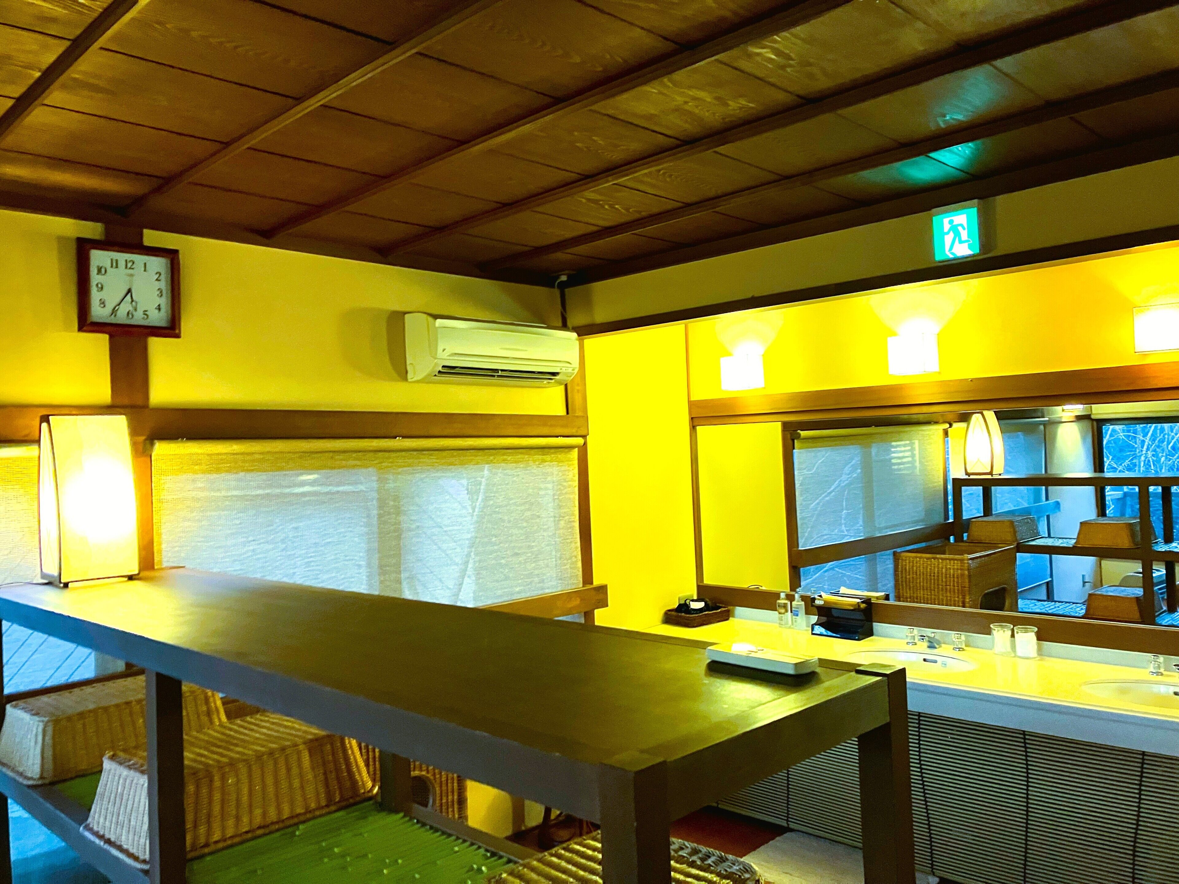 Een hotelkamer met een houten plafond, een klok aan de muur, een airconditioning, een raam met uitzicht en een tafel met lamp.