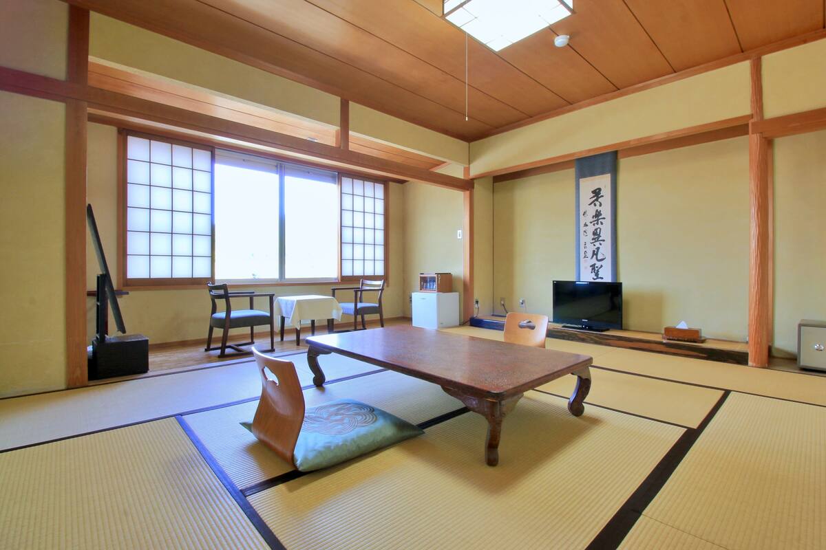 A traditional Japanese room with tatami flooring, a low table, a television, and a sliding door.