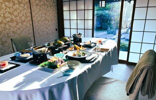 A traditional Japanese-style dining table set with various dishes and utensils, a tatami mat, and a view of a garden through a shoji screen.