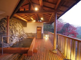 A wooden deck with a hot spring bath, stone wall, and a wooden door leading to a covered area.