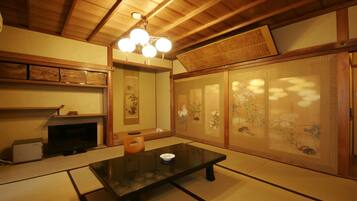 A traditional Japanese room with tatami flooring, a low table, a television, and sliding doors with artwork.