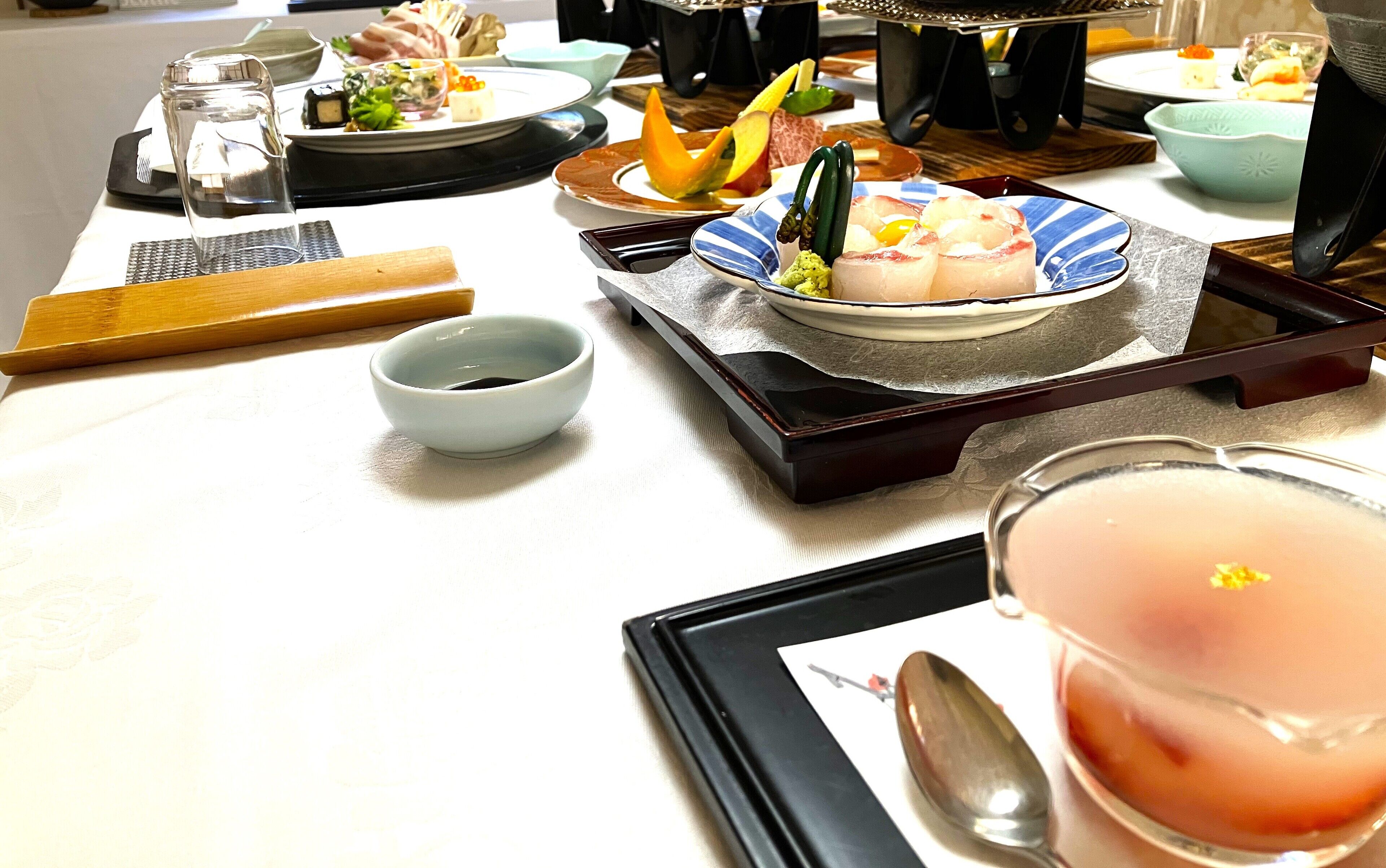 A dining table with various dishes, a small bowl, a tray, and a glass of drink.