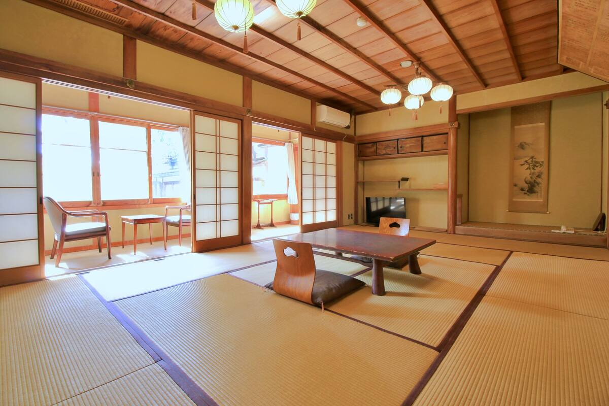 A traditional Japanese room with tatami flooring, a low table, chairs, and sliding doors.